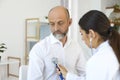 Young female cardiologist listening to senior man`s heartbeat at clinic. Doctor examining elderly patient at office Royalty Free Stock Photo