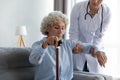 Female nurse help senior lady stand up from couch