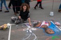 Young female caucasian college student siting on the street and draws a mural with chalk as seen on this date