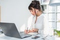 Young female clerk sitting at modern office making notes in her notepad. Employee working on the work table with