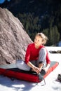 Young female climber putting climbing shoes on before climbing on a boulder outdoors