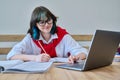 Young female college student sitting at desk in classroom, using laptop, writing in notebook Royalty Free Stock Photo