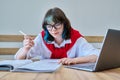 Young female college student sitting at desk in classroom, using laptop, writing in notebook Royalty Free Stock Photo