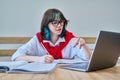 Young female college student sitting at desk in classroom, using laptop, writing in notebook Royalty Free Stock Photo