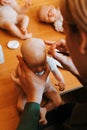 Young female craftsman painting hair on head of newborn caucasian baby doll sitting in home workshop. Royalty Free Stock Photo