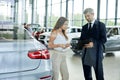 Young female customer asking mature sales manager to help in car dealership. Royalty Free Stock Photo