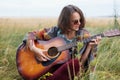 Young female with dark short hair sitting at green grass outdoors playing guitar enjoying nice landscapes singing her favourite so Royalty Free Stock Photo