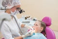 Young female dentist in loupe binoculars checked and curing teeth of child patient sitting in dental chair. Royalty Free Stock Photo