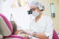 Young female dentist wearing in loupe binoculars checked and curing teeth of child patient sitting in dental chair. Royalty Free Stock Photo