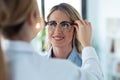 Young female doctor choosing while proving eyeglasses to mature beautiful patient in medical consultation