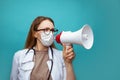 Young female doctor in face mask shouting into megaphone on blue background Royalty Free Stock Photo