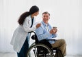 Young female doctor helping senior handicapped man in wheelchair, taking care of older patient at retirement home Royalty Free Stock Photo