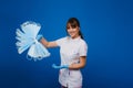 A young female doctor holds a lot of masks in her hands. A nurse poses on a blue background