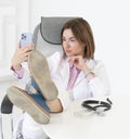 Young female doctor with legs on desk position relaxing and taking photo with smartphone instead of working Royalty Free Stock Photo