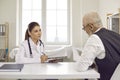 Young female doctor listening to her senior male patient during appointment at clinic Royalty Free Stock Photo