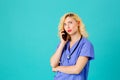 Young female doctor or nurse wearing blue scrub uniform and stethoscope talking on mobile phone