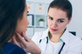 Young concentrated female doctor palpating lymph nodes of a patient. Doctor touching the throat of a patient.