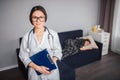 Young female doctor stand in room and look on camera. She hold plastice tablet in hands and stethoscope around neck