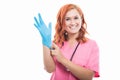 Young female doctor with stethoscope putting blue sterile glove