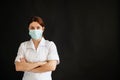 Young female doctor in uniform in a medical mask on a black background. A nurse in a department store folded her arms Royalty Free Stock Photo