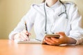 Young female doctor using modern smartphone in the hospital, seeking information in the internet.