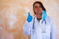 Young female doctor with white lab coat blue gloves and medical mask and stethoscope around her neck doing everything ok Royalty Free Stock Photo