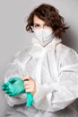 A young female doctor in a white protective disposable jumpsuit puts on green latex gloves. Gray background Royalty Free Stock Photo