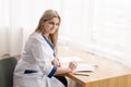 Young female doctor working desk in doctor`s room writing.