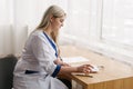 Young female doctor working desk in doctor`s room writing. Royalty Free Stock Photo