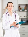 Positive young female doctor takes important notes while standing in a office Royalty Free Stock Photo