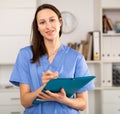 Positive young female doctor takes important notes while standing in a office Royalty Free Stock Photo