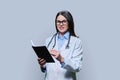 Young female doctor writes in notebook, on gray studio background. Royalty Free Stock Photo