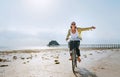 Young female dressed light summer clothes joyfully threw up her hand riding old vintage bicycle with front basket on the low tide Royalty Free Stock Photo