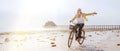 Young female dressed light summer clothes joyfully threw up her hand riding old vintage bicycle with front basket on the low tide Royalty Free Stock Photo