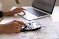 Young female electronic bank client using calculator in paperwork