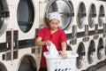 Young female employee carrying laundry basket with washing machines in background