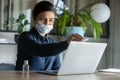 Female employee in face mask disinfect laptop with sanitizer