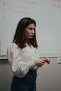 Young female english language teacher with a red marker in a white blouse standing in front of a white board Royalty Free Stock Photo