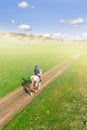 Young female equestrian riding horse along rural countryside. Rider on horseback going through green hillside.Travelling along. Royalty Free Stock Photo