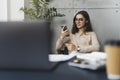 Young female executive sitting at workplace at lunch time and listening to music on smartphone using earphones. Girl using mobile