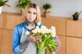 young female florist in apron holding beautiful tulips in vase and looking