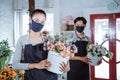 young female florist wearing apron and face mask holding bucket flower smiling looking at camera. working in flower shop Royalty Free Stock Photo