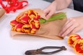 Young female florist is wrapping a red color tulip flower bouquet for Mother`s Day gift with tie ribbon bow over a white table Royalty Free Stock Photo