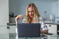 young female freelancer holding eyeglasses and using laptop while working