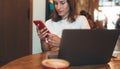 Young female freelancer holding smartphone using laptop in cafe, hipster girl writing on mobile phone, businesswoman working Royalty Free Stock Photo