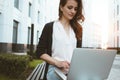 Young female freelancer making labor market research on modern laptop, sits on outdoors in urban street. Woman student work on mob