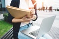 Young female freelancer making labor market research on modern laptop, sits on outdoors in urban street