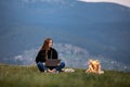 Young female freelancer working on laptop in the mountains in the evening. Tourist girl sitting near campfire and having fun. Copy