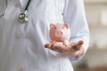 Young female general practitioner holding piggy bank in hands.