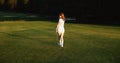 A young female golfer is walking along the golf course. Back view